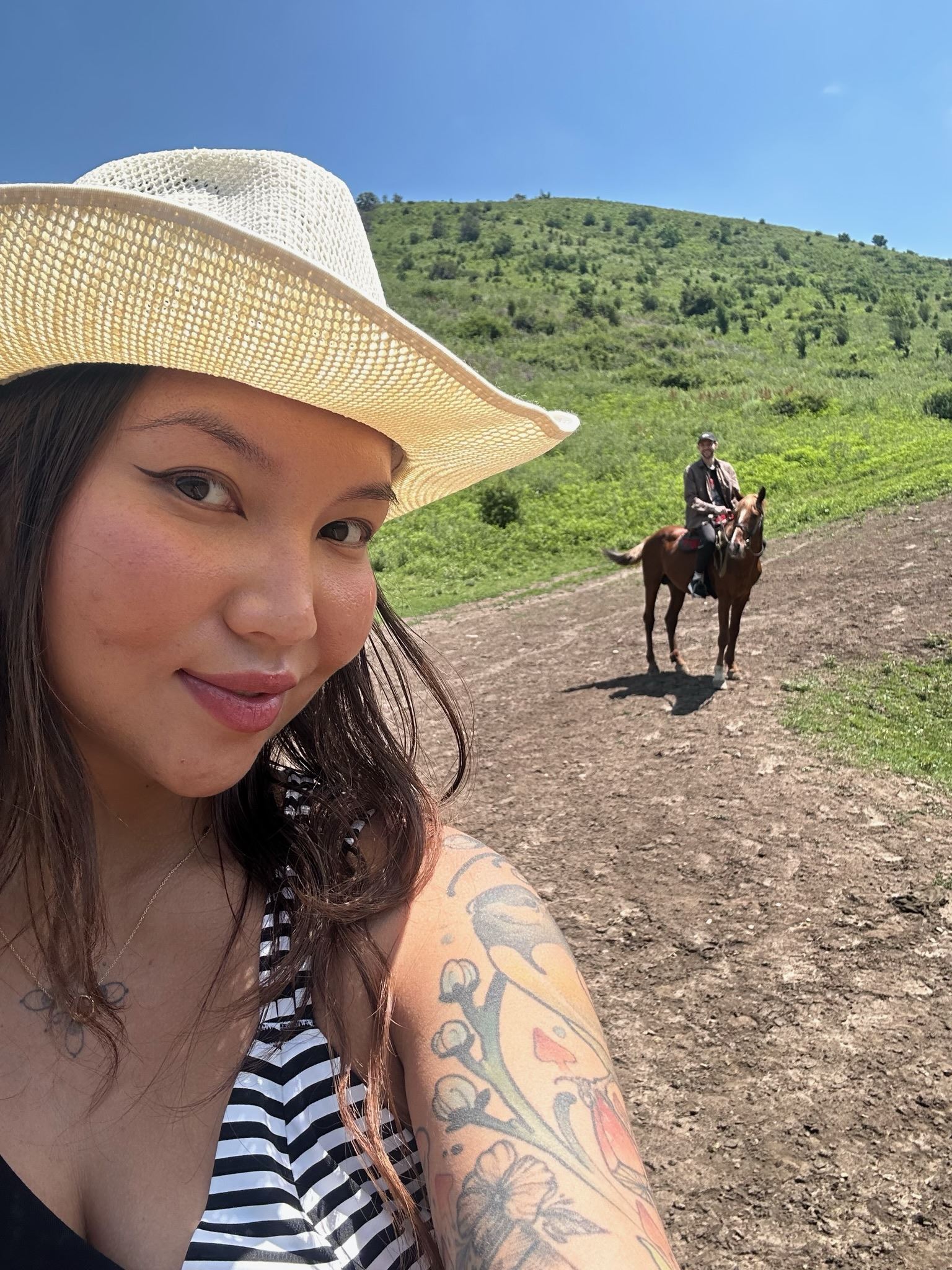 Dinara on a trail in the foothills, a rider on horseback in the background