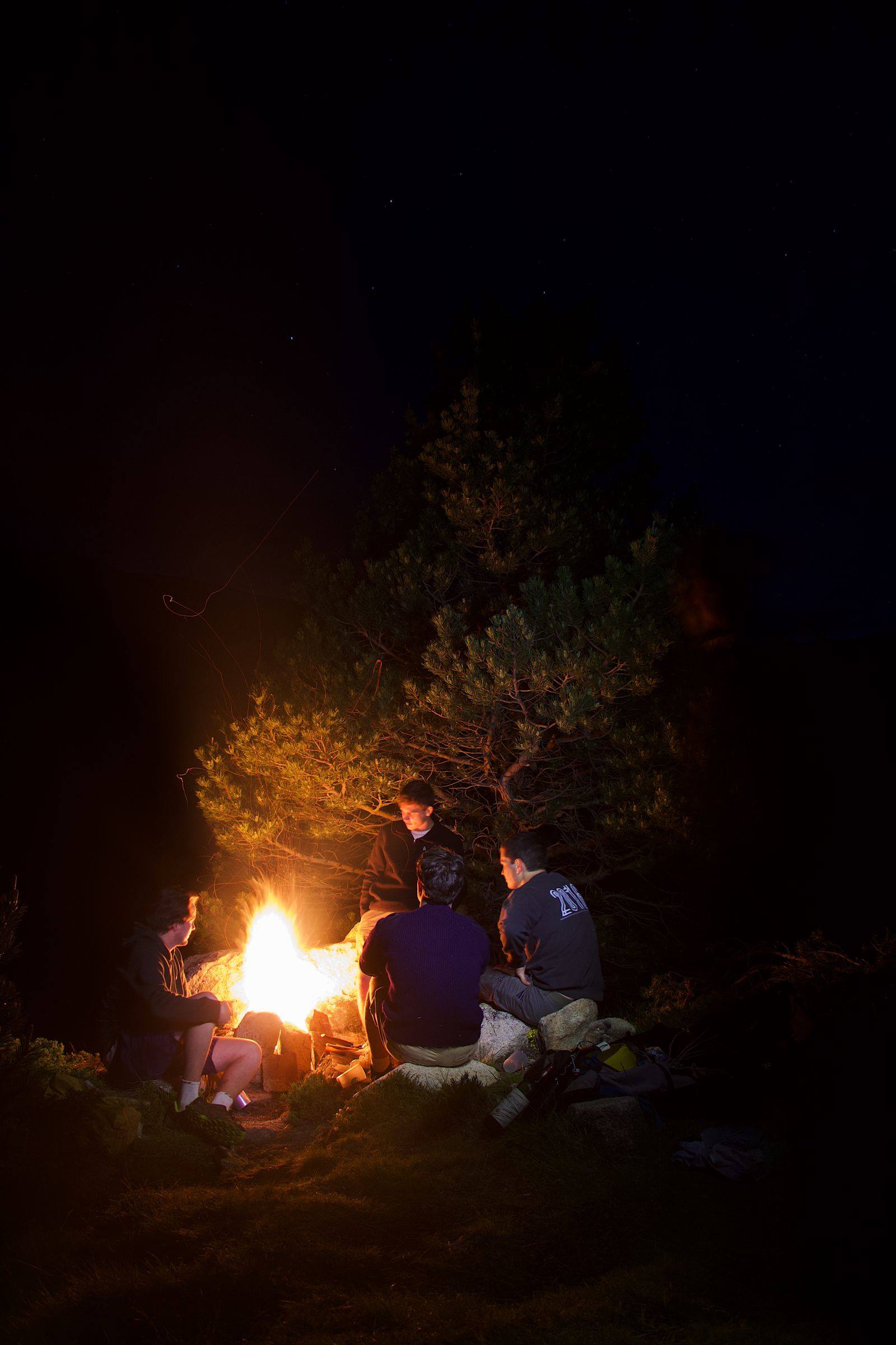 A group of friends gathered around a campfire at night, warm firelight