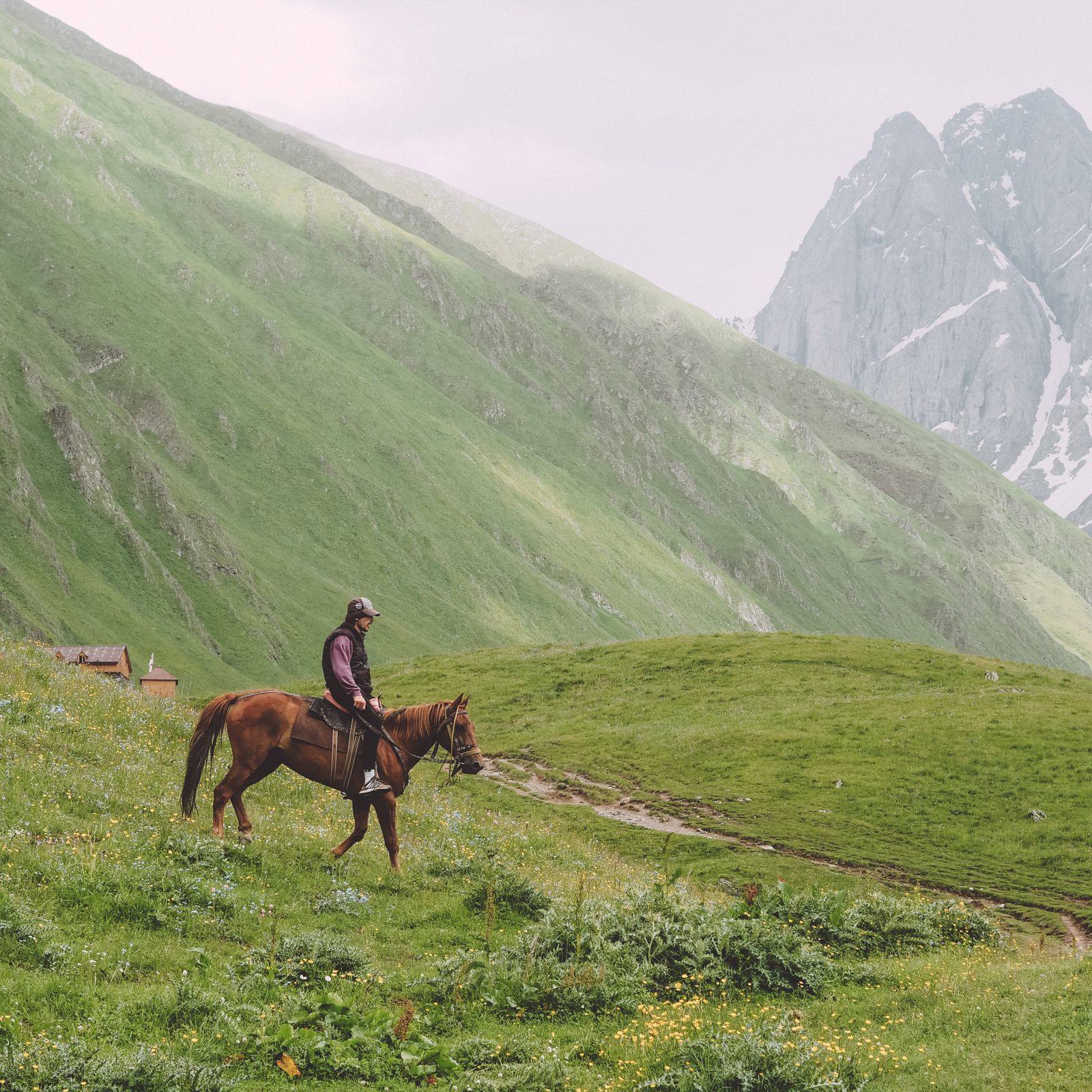 A rider on horseback moving through a lush green mountain valley